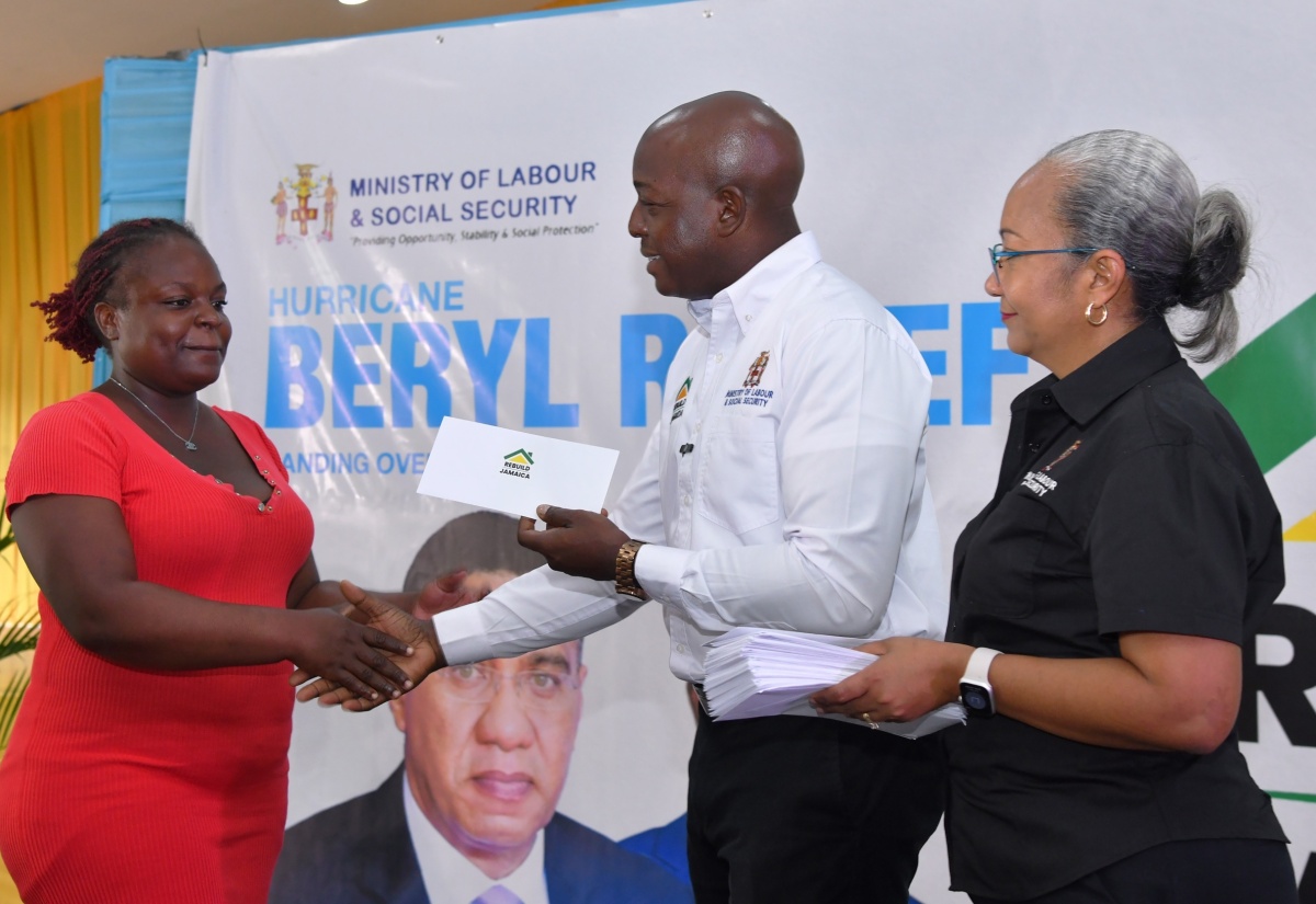 Minister of Labour and Social Security, Hon. Pearnel Charles Jr., presents a cheque to Belinda Bowen, during the handover of cash grants to persons across the parish of St. Catherine whose houses were damaged by Hurricane Beryl. The ceremony was held on August 27, at the HEART College of Construction Services in Portmore. At right is Permanent Secretary in the Ministry, Colette Roberts Risden.

