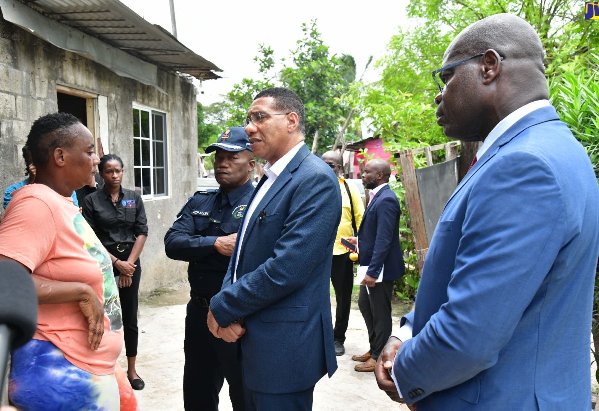 Prime Minister, the Most Hon. Andrew Holness (centre), converses with the mother (left) of one of the eight persons murdered in Cherry Tree Lane, Clarendon, on Sunday night (August 11). He was accompanied by Acting Commissioner of Police, Fitz Bailey (right), and Assistant Commissioner of Police, Calvin Allen. The Prime Minister visited the area on Monday (August 12), where he met with family members and community persons.

