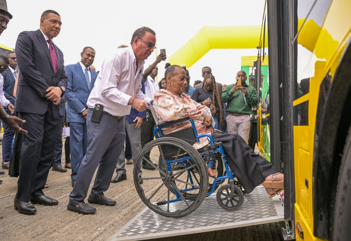 Prime Minister the Most Hon. Andrew Holness (left), and Minister of Finance and the Public Service, Dr. the Hon. Nigel Clarke (second left), observe as Minister of Science, Energy, Telecommunications and Transport, Hon. Daryl Vaz, assists President of the Combined Disabilities Association, St. Catherine, Christine Keene, in maneuvering her wheelchair onto a ramp affixed to one of the Jamaica Urban Transit Company’s new compressed natural gas (CNG) buses. The occasion was Tuesday’s (August 27) handover ceremony for the 100 new CNG buses acquired for the JUTC at the State entity’s Portmore Depot in St. Catherine.

