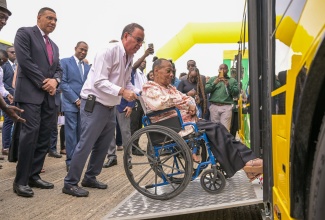 Prime Minister the Most Hon. Andrew Holness (left), and Minister of Finance and the Public Service, Dr. the Hon. Nigel Clarke (second left), observe as Minister of Science, Energy, Telecommunications and Transport, Hon. Daryl Vaz, assists President of the Combined Disabilities Association, St. Catherine, Christine Keene, in maneuvering her wheelchair onto a ramp affixed to one of the Jamaica Urban Transit Company’s new compressed natural gas (CNG) buses. The occasion was Tuesday’s (August 27) handover ceremony for the 100 new CNG buses acquired for the JUTC at the State entity’s Portmore Depot in St. Catherine.

