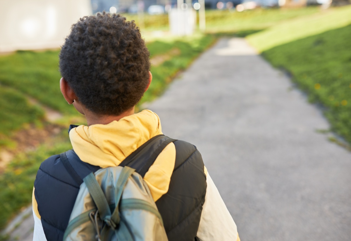 Rear view of child carrying backpack going home from school.