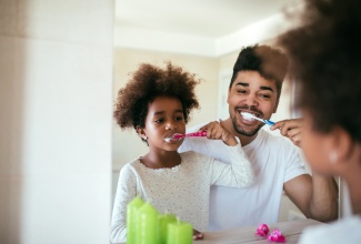 Father and daughter brushing teeth in bathroom. 