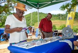 Community members, Etta Thompson and Reverend Leon West, peruse various health ‘Get The Facts’ publications at the Jamaica Information Service (JIS) booth during the Blue Mountain Seventh Day Baptist Church’s recent health and wellness fair in Manchester.

