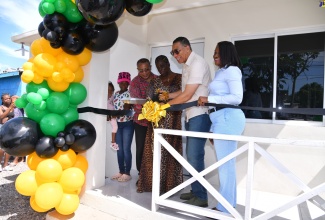 Prime Minister, the Most Hon. Andrew Holness (second right), and Permanent Secretary in the Ministry of Economic Growth and Job Creation, Arlene Williams (right), cut a ribbon during Friday’s (September 6) handover ceremony for a new housing unit at Lot 129 Callaloo Mews, St. Andrew Western, which was developed under the New Social Housing Programme (NSHP). They are joined by Member of Parliament for the constituency, Anthony Hylton (second left), NSHP beneficiary and recipient of the unit, Karen Francis (centre), and her granddaughter, Trishanna Carter (left).

