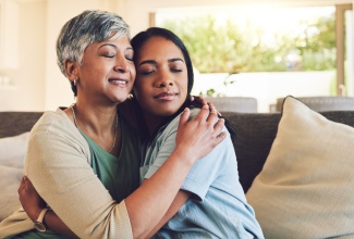 Senior woman hugging her daughter in the living room. 