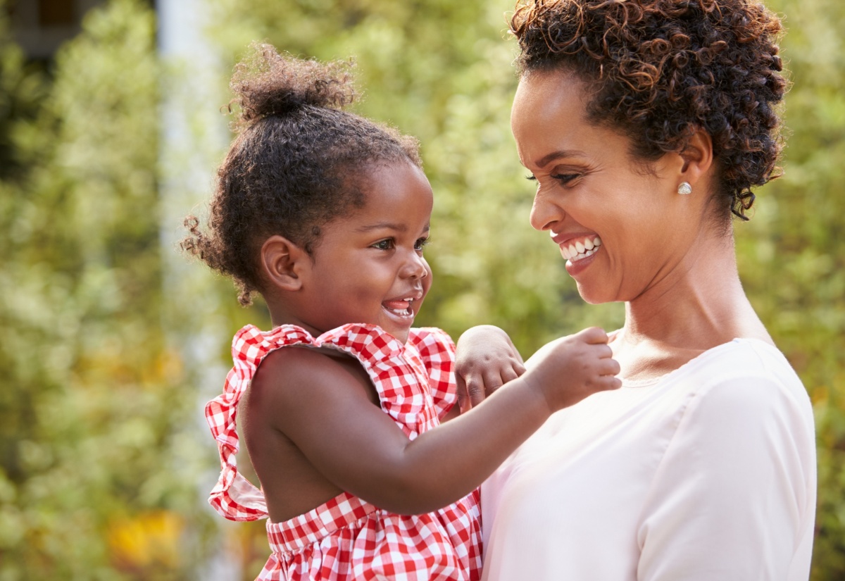 Young mother holds baby girl in garden.