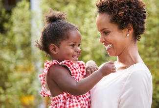 Young mother holds baby girl in garden.